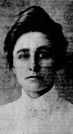 A young white woman with dark hair piled in a bouffant updo, wearing a white blouse with a high collar