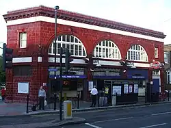 A red-bricked building with a rectangular, dark blue sign reading "TUFNELL PARK STATION" in white letters all under a blue sky with white clouds