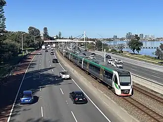 Six car electric multiple unit train running on tracks within the median strip of a freeway