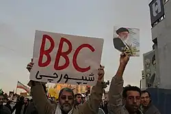 عکس از شعار نویسی یک منتقد شبکه بی بی سی در یک راهپیمایی اعتراضی، مقابل خانه یوسف صانعی در سال ۱۳۸۸ (نوشته روی پلاکارد: بیبیسی شیپورچی )