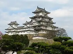 A multistoried white castle donjon with several small towers and a main tower on a platform of stone.