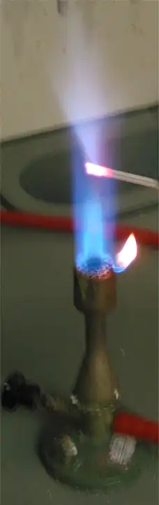 شعلهای که یک میله فلزی کوچک در آن نفوذ کرده است؛ شعله در نزدیکی میله آبی کمرنگ است.
