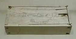 White rectangular box with small cracks and a long line of hieroglyphs along the entire length of the lid, at its centre