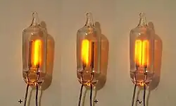عکسی از سه لولهٔ شیشه‌ای که هر کدام شامل دو سیم موازی با هم هستند. در محفظهٔ شیشه‌ای سمت چپ سیم سمت راست با رنگ نارنجی می‌درخشد، در محفظهٔ میانی سیم سمت چپ روشن شده و در محفظهٔ سمت راست هر دو روشن هستند.