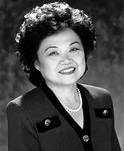 Black and white photographic portrait of a woman in a suit adorned with a pearl necklace