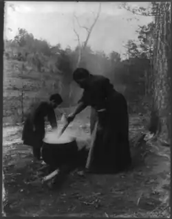 یک زن سیاه‌پوست آمریکایی و فرزندش بیرون خانه نزدیک پاتیلی که آب آن در حال جوشیدن است،ایستاده‌اند. حدود. ۱۹۱۰