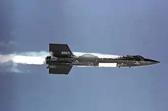 Black rocket aircraft with stubby wings and short vertical stabilizers above and below tail unit